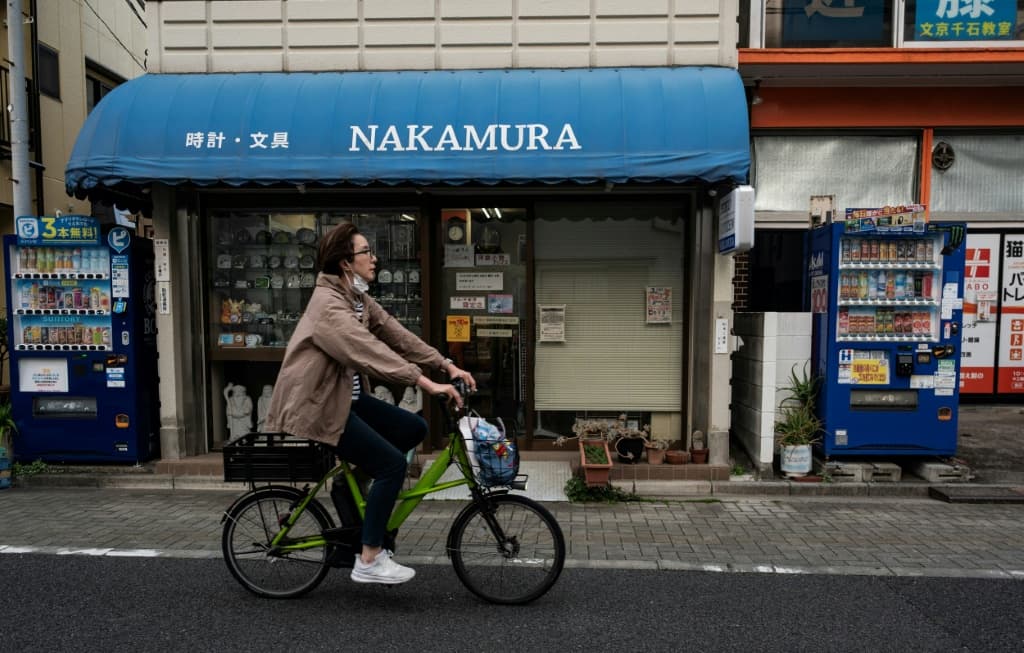 A woman cycles past two vending machines next to a clock shop in Tokyo's Bunkyo district on April 14, 2026