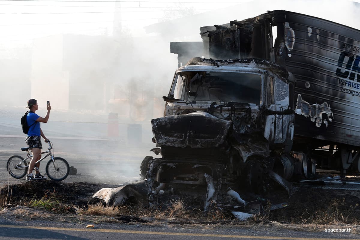 ชายคนหนึ่งถ่ายรูปรถบรรทุกที่ถูกเผาบนทางหลวงใกล้เมืองอากาตลัน เด ฮัวเรซ รัฐฮาลิสโก ประเทศเม็กซิโก เมื่อวันที่ 22 กุมภาพันธ์ 2026 Photo by ULISES RUIZ / AFP